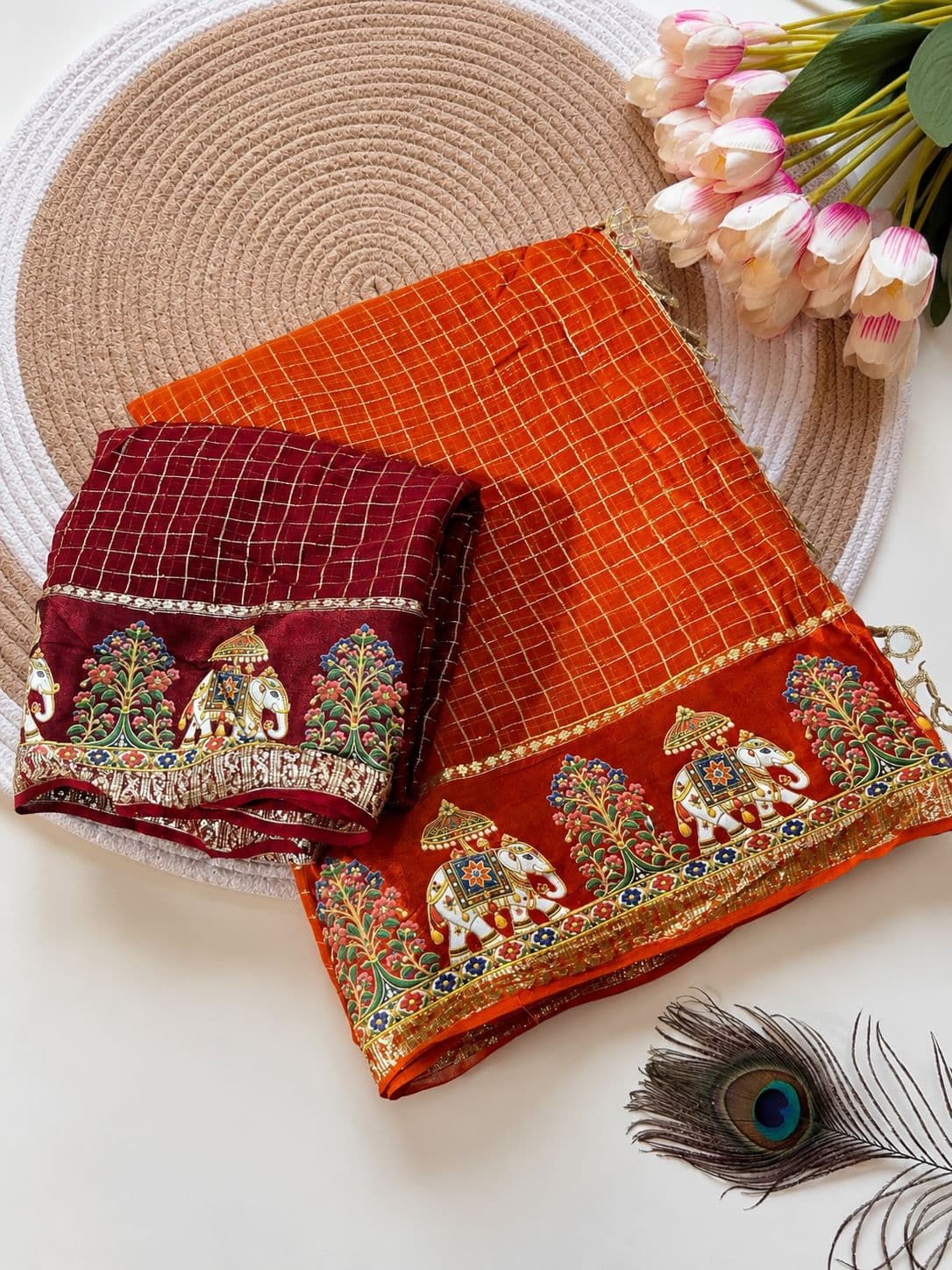 Folded orange and maroon Kalamkari silk sarees with gold zari check pattern and elephant motif border